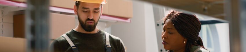 Quality assurance manager and warehouse laborer preparing orders for delivery, using digital device to check shipping info while scanning labels on parcels in retail deposit